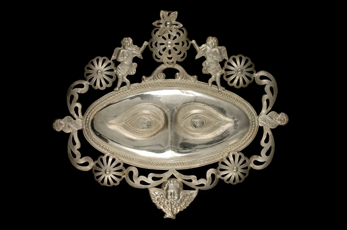 Ex-voto représentant des yeux, Naples, Italie, avant 1962. Bordure ajourée ornée de motifs floraux et de cinq anges, argent, 15,7 cm x 17,8 cm x 0,66 cm. Collection d’ethnologie d’Europe, Muséum national d’histoire naturelle, en dépôt au Mucem © MNHN, photo Mucem