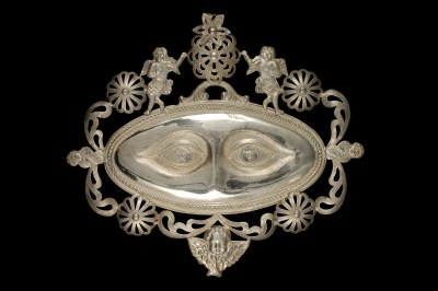 Ex-voto représentant des yeux, Naples, Italie, avant 1962. Bordure ajourée ornée de motifs floraux et de cinq anges, argent, 15,7 cm x 17,8 cm x 0,66 cm. Collection d'ethnologie d'Europe, Muséum national d'histoire naturelle, en dépôt au Mucem © MNHN, photo Mucem